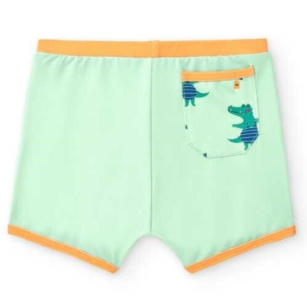Boxer de praia infantil BtBox verde-água com acabamentos laranja e bolso traseiro com crocodilos azuis estampados.
