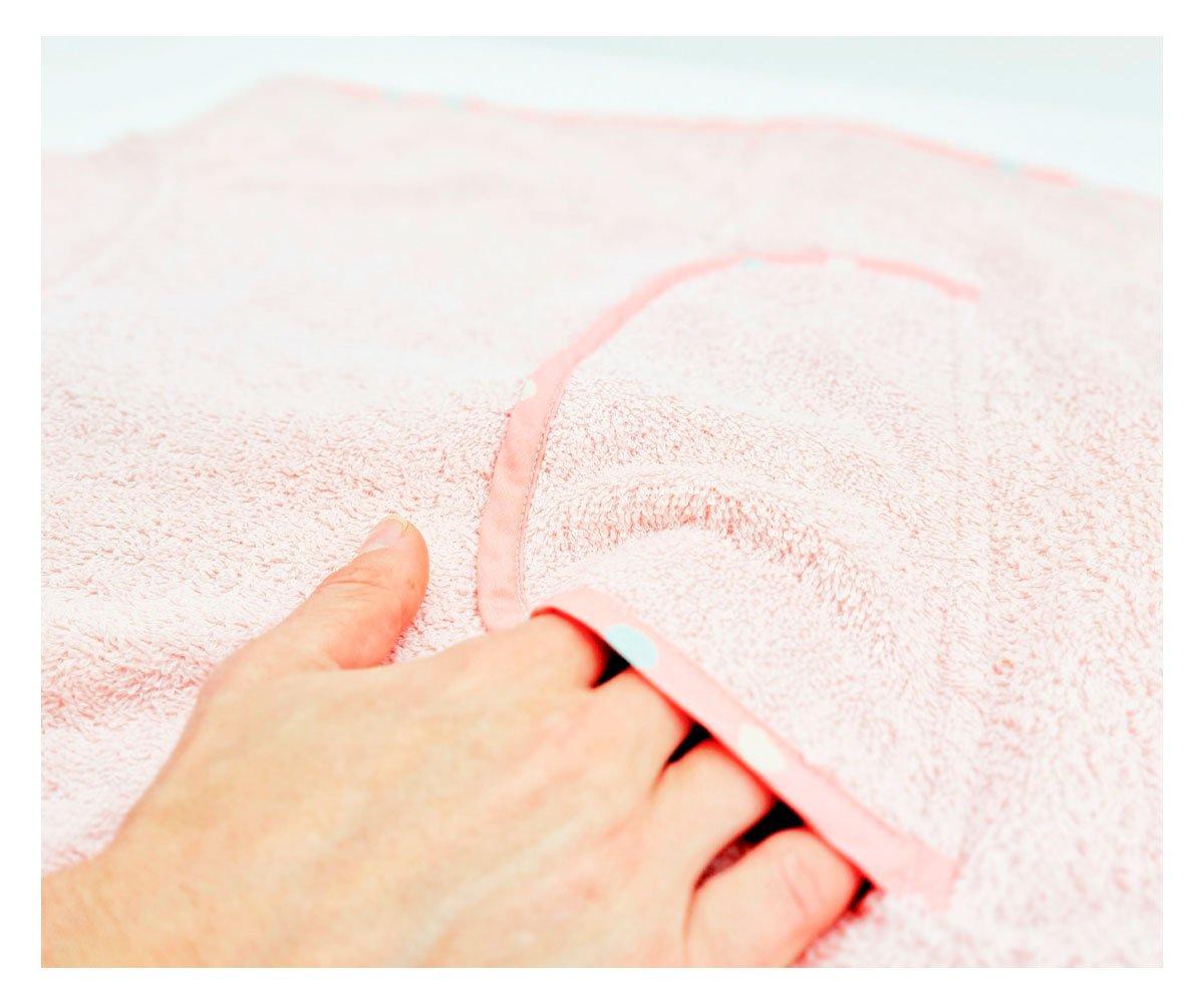 Detalhe da textura felpuda do algodão orgânico do poncho Btbox, com uma mão a tocar o tecido e o bolso frontal.