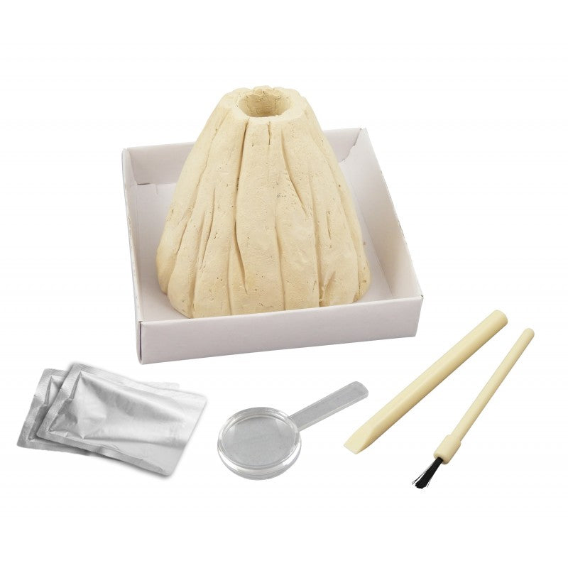 Componentes do kit Mini Vulcão Buki: molde de vulcão de gesso, pacotes de reagentes, colher, cinzel e pincel, dispostos numa caixa branca.