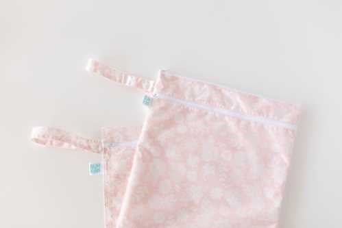 Duas bolsas impermeáveis Bumkins com padrão floral 'Lace' empilhadas sobre um fundo branco, mostrando o fecho e a alça.