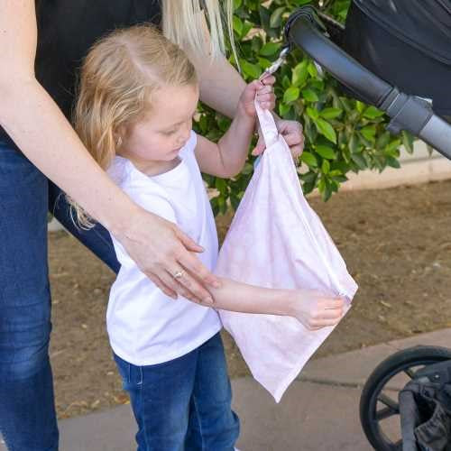 Criança e adulto a prender a bolsa impermeável Bumkins com fecho de pressão ao carrinho de bebé, demonstrando uso prático.