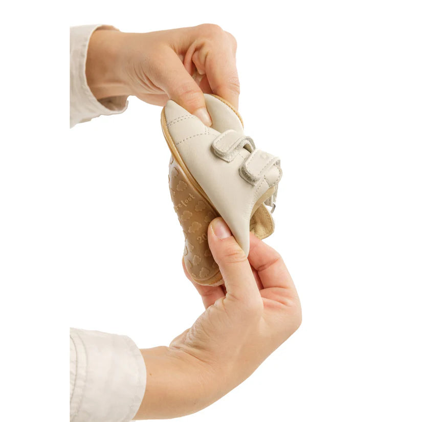 Demonstração da flexibilidade da sapatilha Bunny Barefoot Coala Rosa Perolado, dobrada pelas mãos para mostrar a sola super flexível.