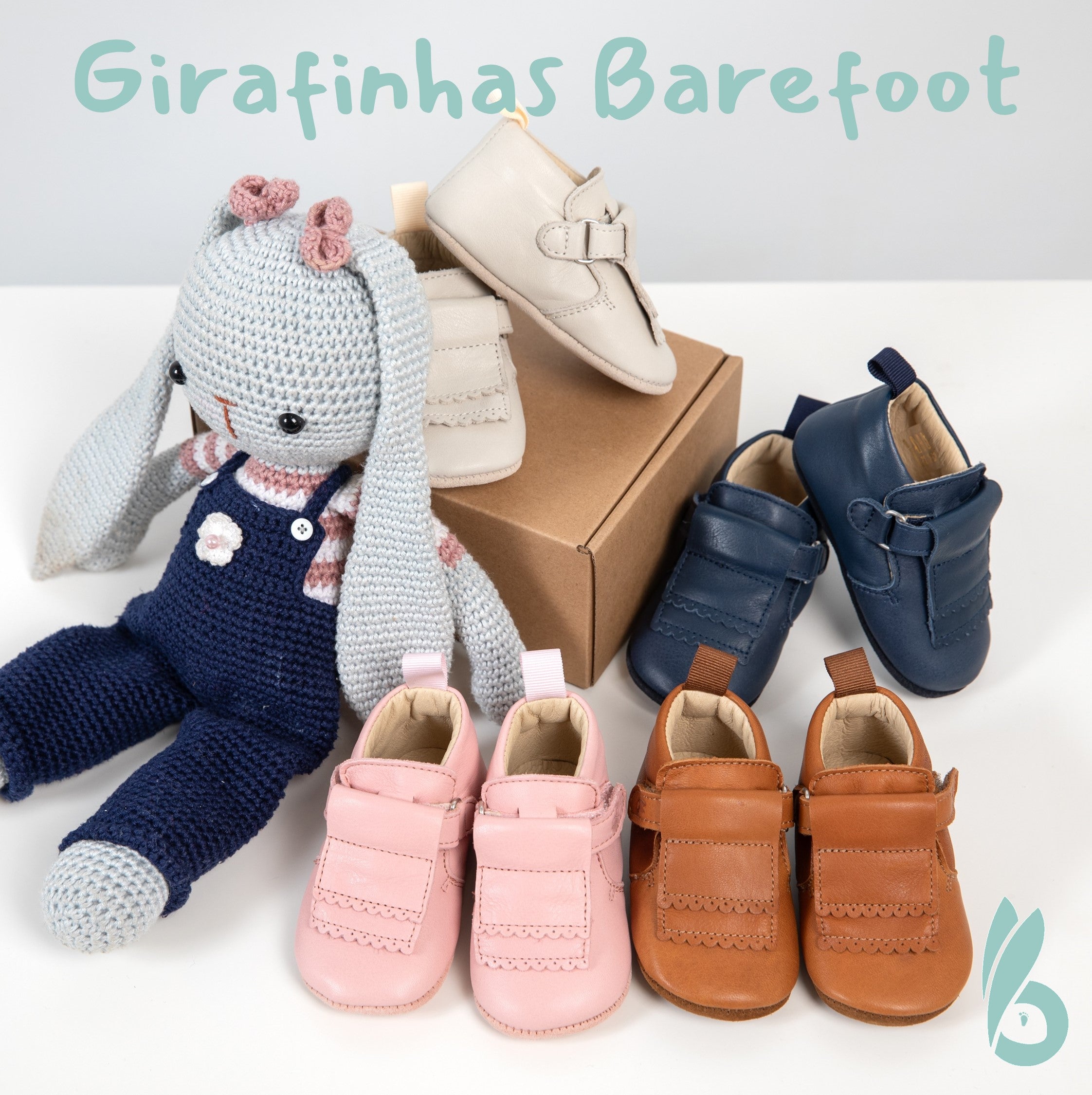 Apresentação de vários pares de sapatinhos "Girafinhas Barefoot" em diferentes cores (rosa, bege, azul, castanho) ao lado de um boneco de coelho de croché, sobre uma caixa de cartão.