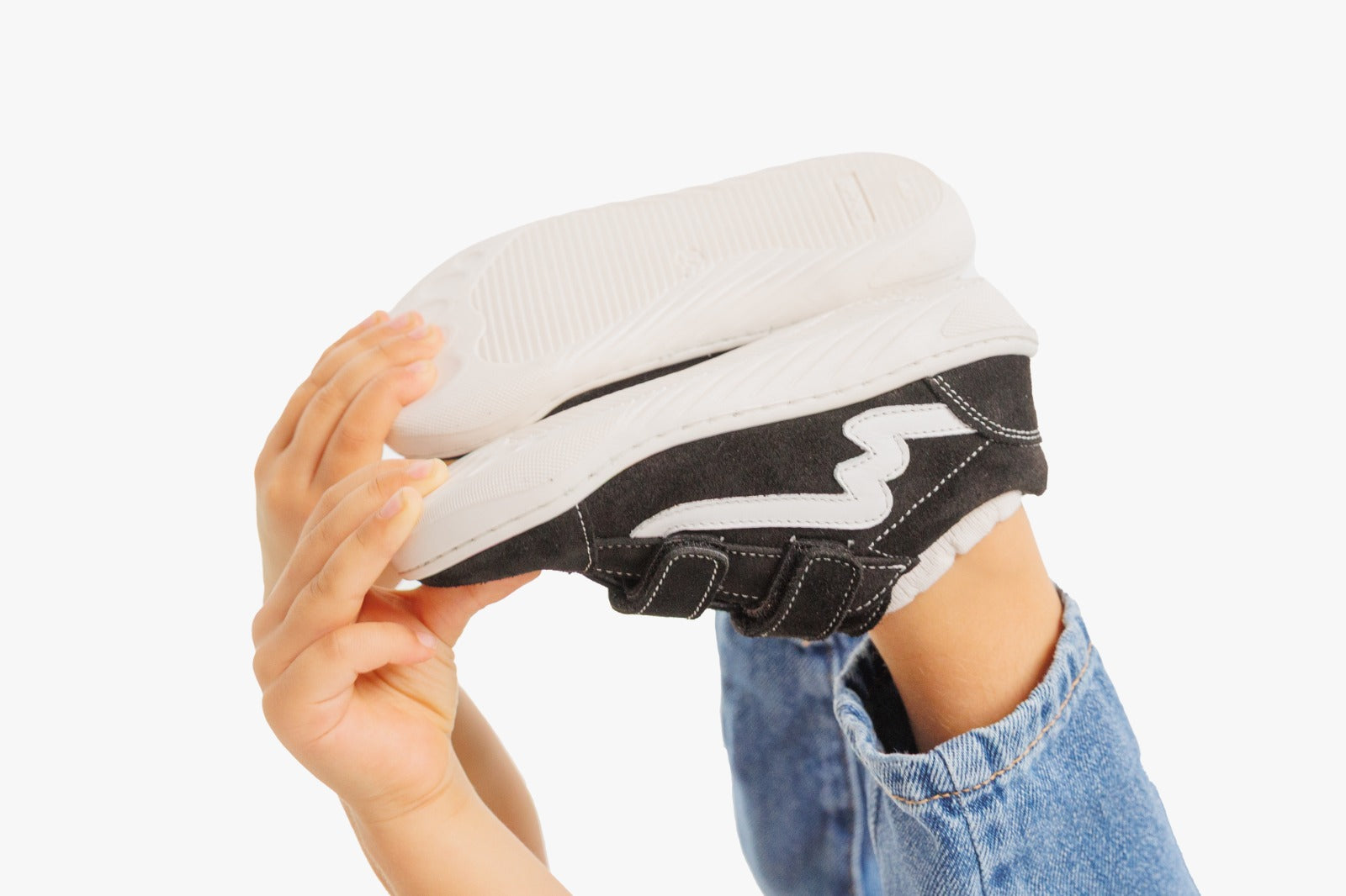 Demonstração da flexibilidade da sapatilha Bunny Barefoot Zebra Preto, sendo dobrada por mãos infantis, exibindo a sola branca fina.