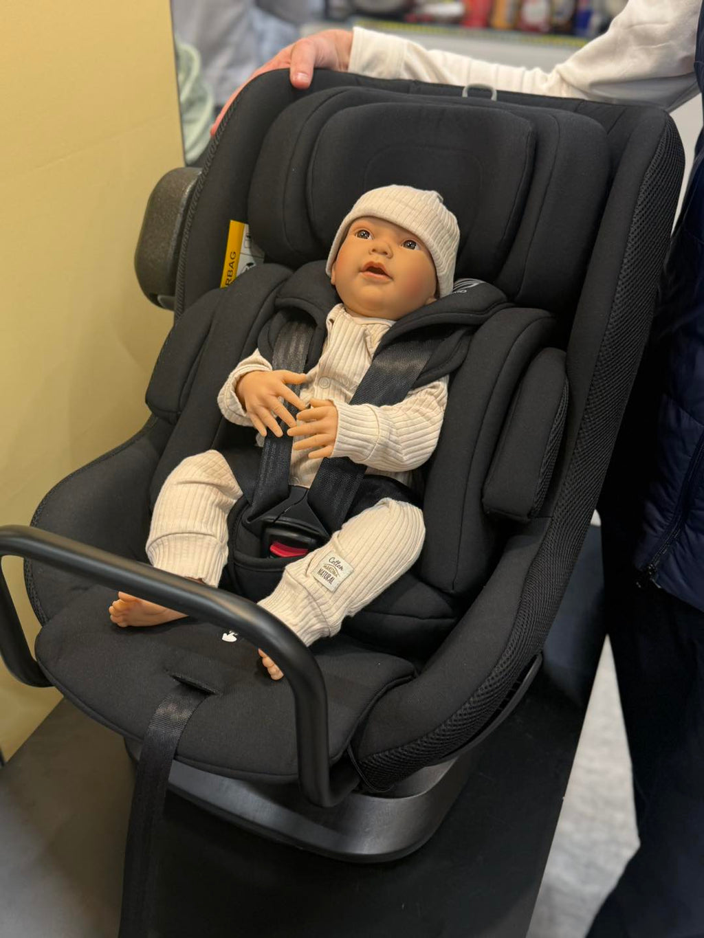 Vista frontal detalhada da cadeira auto Axkid Minikid CORE com boneco bebé, mostrando o arnês de segurança e o apoio de cabeça.