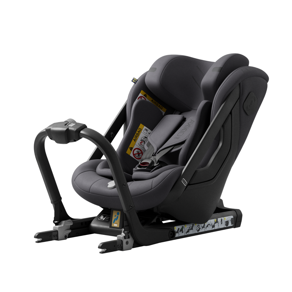 Cadeira auto Axkid ONE 3 cinzenta escura, instalada contra a marcha, com base ISOFIX visível e arnês de 5 pontos, isolada em fundo preto.