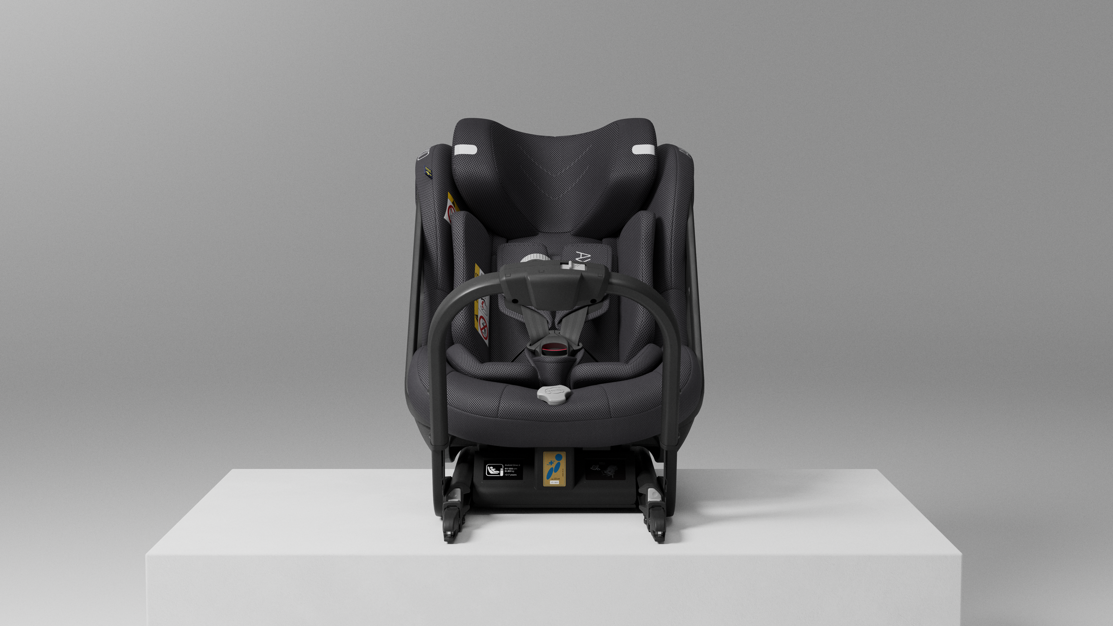 Vista frontal da Cadeira Auto Axkid ONE 3 MESH preta, mostrando o arnês de 5 pontos e o apoio de cabeça, sobre um pedestal branco.
