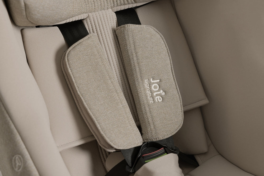 Detalhe dos redutores de arnês acolchoados em tecido bege claro com o logótipo "Joie Signature" bordado na Cadeira Auto i-Harbour.