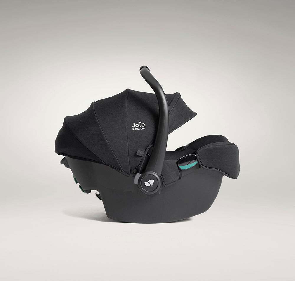 Cadeira auto ovo Joie i-Starter preta, vista de lado, com a pega de transporte inclinada para trás e a capota parcialmente aberta.