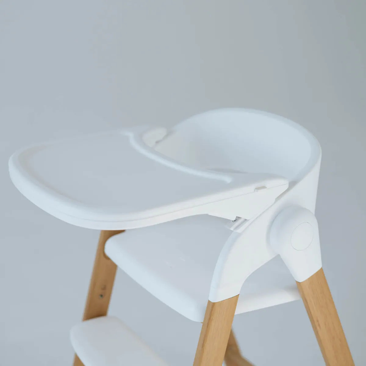 Detalhe da parte superior da cadeira de refeição Love & Carry Flex branca, mostrando o tabuleiro ajustável e o assento com o redutor.