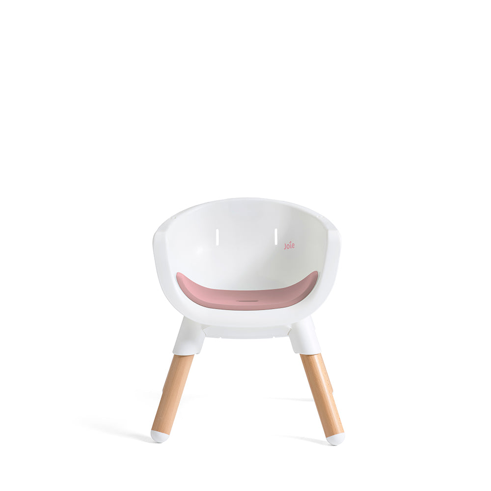 Cadeira evolutiva Joie Chestnut convertida em cadeira júnior baixa, vista frontal. Assento branco com almofada rosa e pernas curtas de madeira. Logótipo Joie visível.