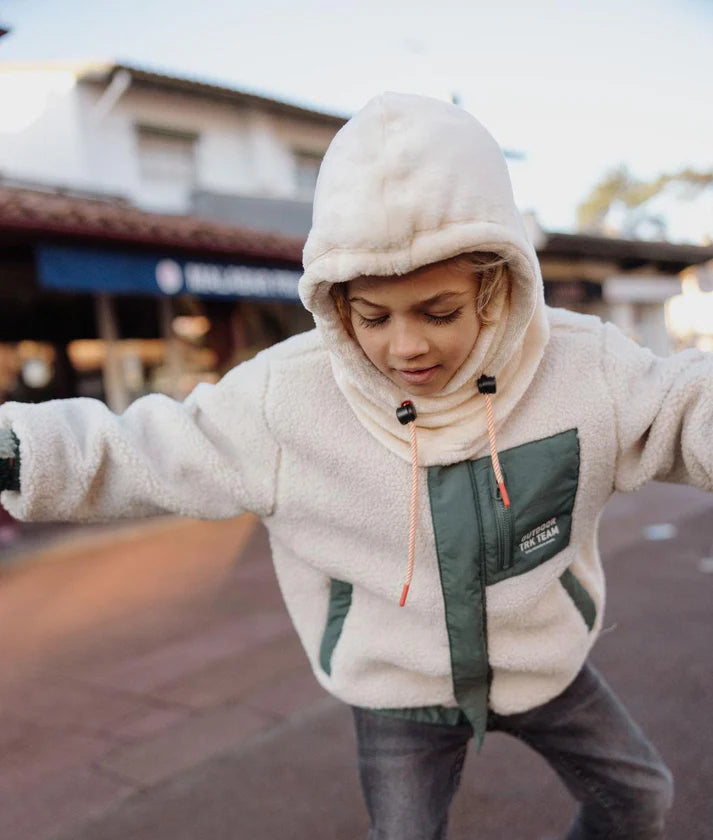 Criança ativa a brincar ao ar livre com o gorro Hello Hossy Warmy Cream com capuz, para proteção e liberdade de movimentos.
