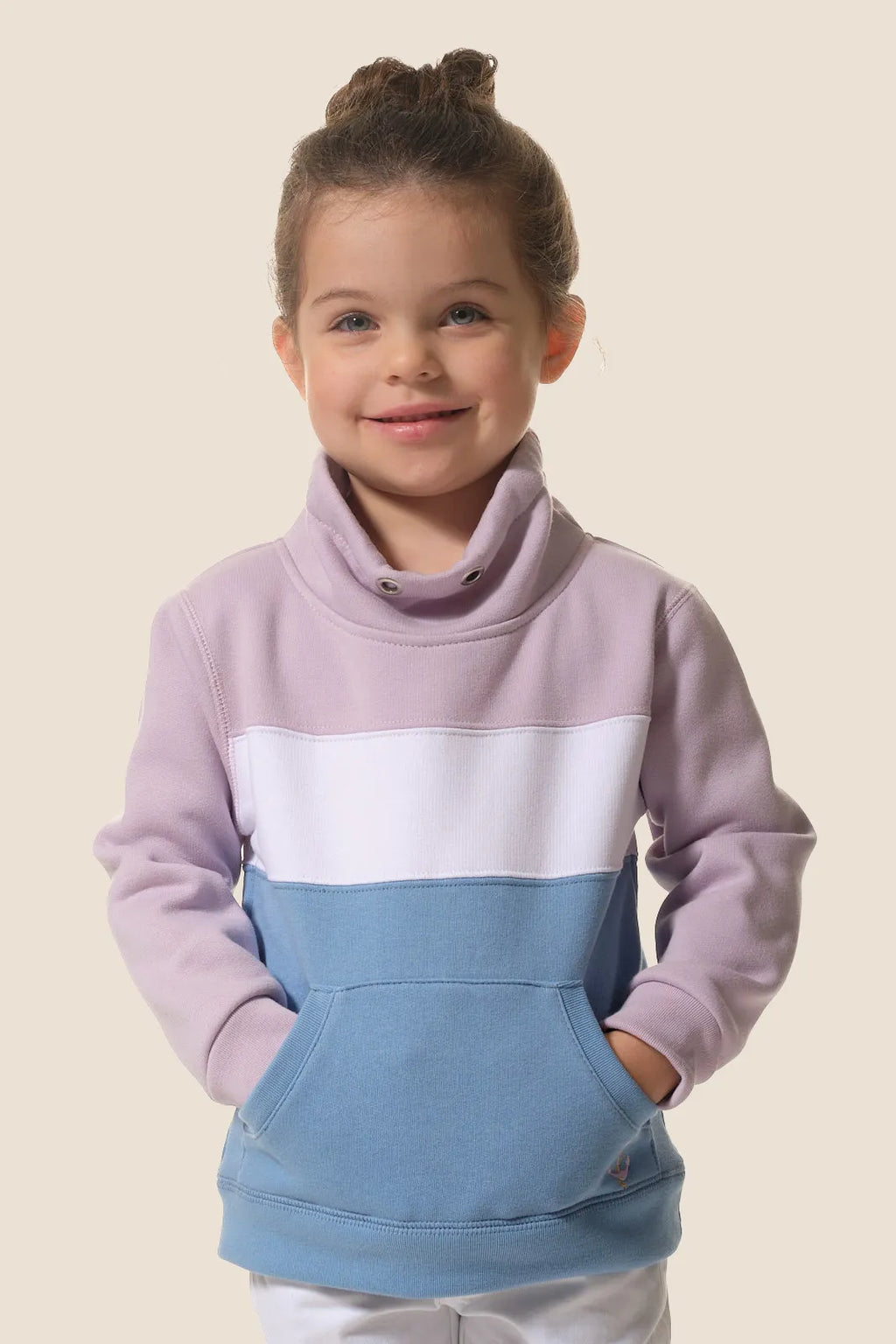 Menina sorridente vestindo a camisola cardada Hublot com gola alta, exibindo o padrão de blocos de cor lilás, branco e azul.