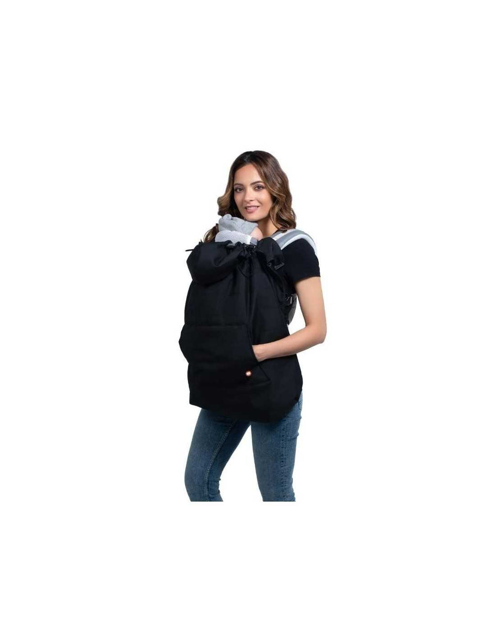 Mulher sorridente a usar a capa Wombat preta para transporte de bebé na frente, com as mãos no bolso frontal.
