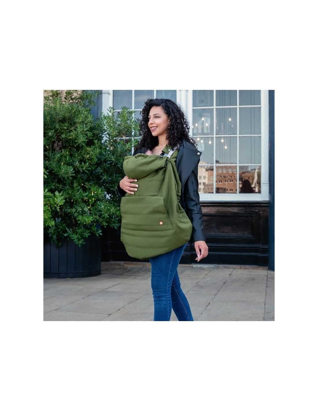 Mãe sorridente a usar a capa Wombat verde-escura para babywearing, protegendo o bebé do vento e da chuva em ambiente urbano.