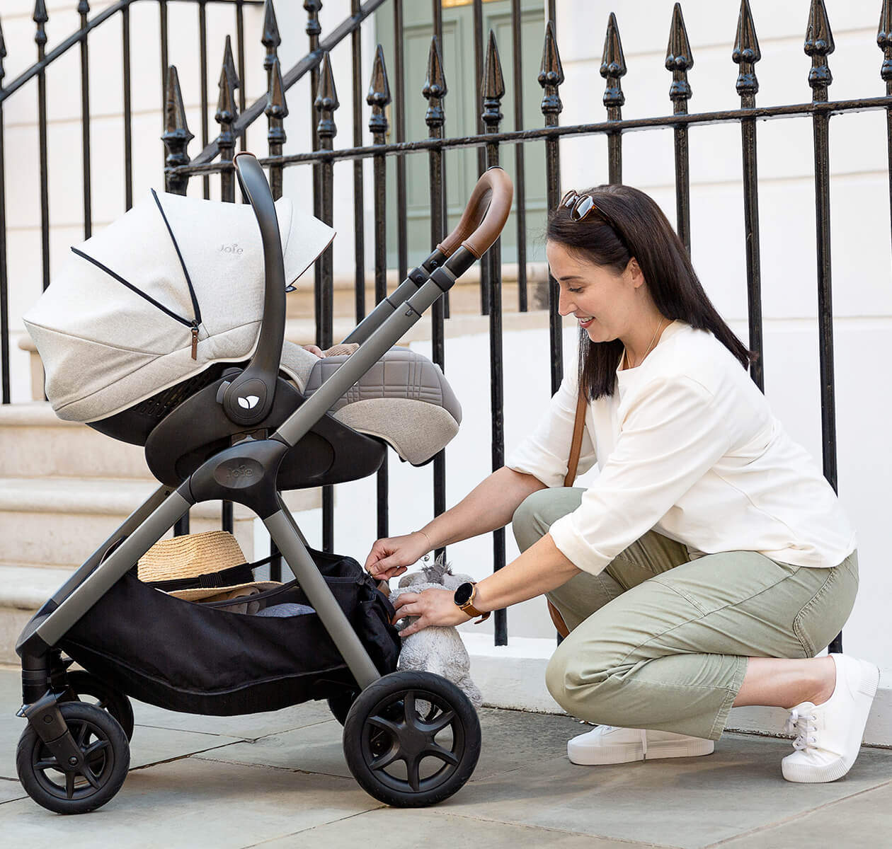 Mãe a organizar o cesto de arrumação do carrinho de bebé Joie Signature Finiti Oyster, com um bebé a descansar no assento. O carrinho destaca-se pelo seu design elegante, estrutura leve e manobrabilidade suave, ideal para passeios urbanos com conforto e praticidade.

