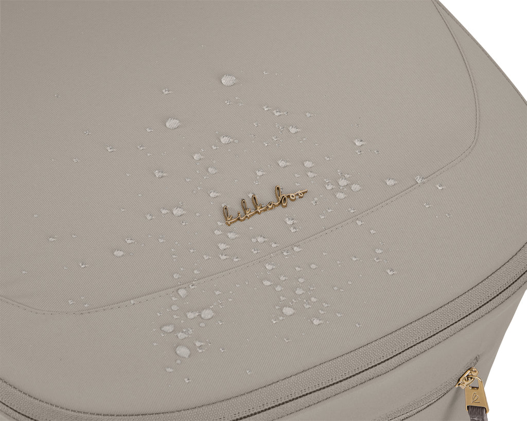 Close-up do tecido do capazo do carrinho Goya Platinum, mostrando gotas de água a escorrer devido à sua impermeabilidade, com o logótipo dourado visível.