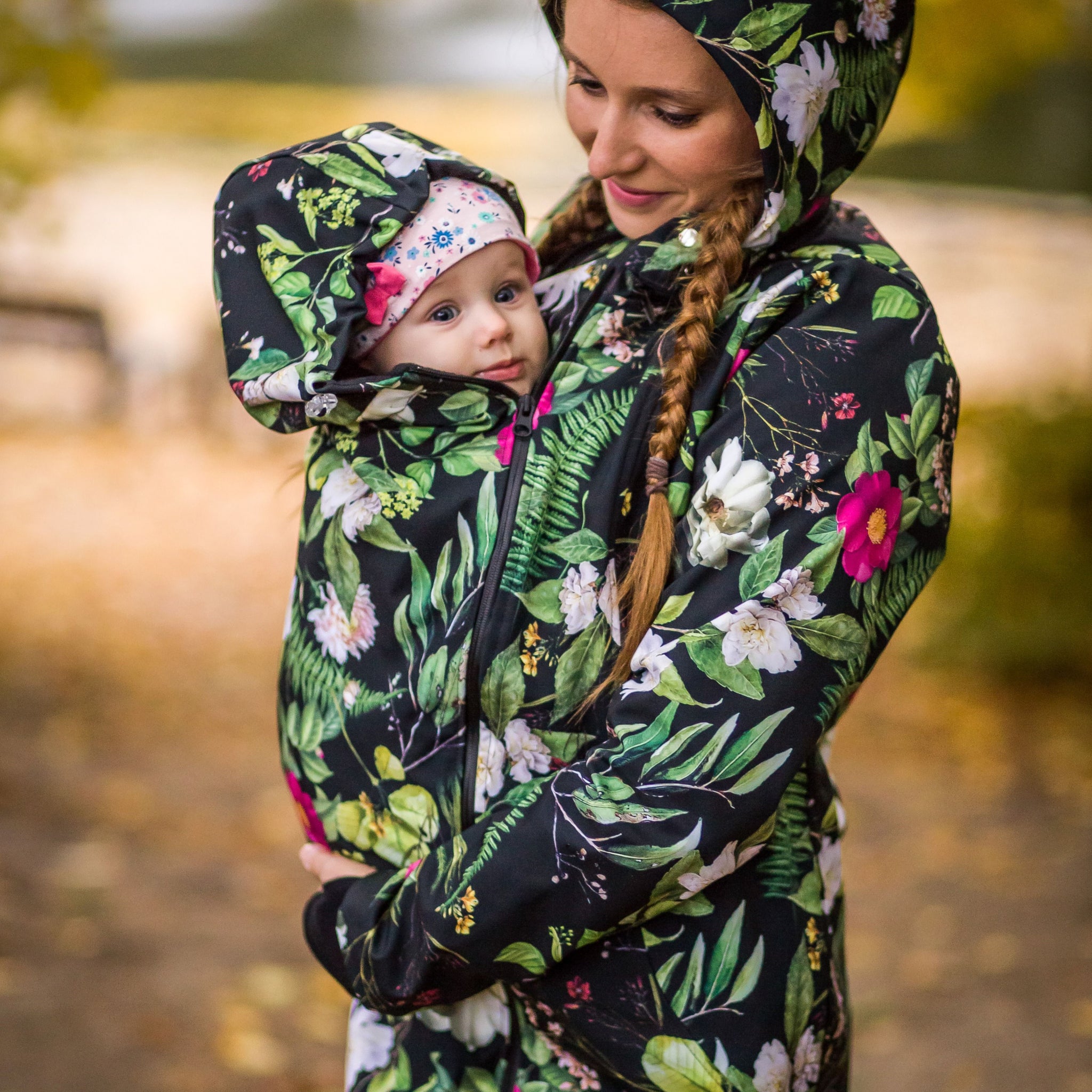 Mãe a usar um casaco de babywearing acolchoado, com padrão floral, protegendo o bebé do frio. Peça prática e quente, perfeita para babywearing no inverno com conforto e estilo.