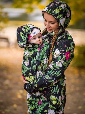 Mãe a usar um casaco de babywearing acolchoado, com padrão floral, protegendo o bebé do frio. Peça prática e quente, perfeita para babywearing no inverno com conforto e estilo.