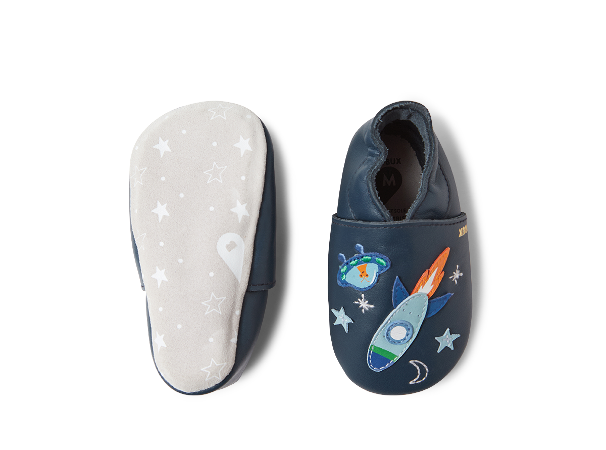 Um sapato Bobux Cosmic Rocket Soft Sole em azul-marinho, visto de cima, e a sola macia do outro sapato com padrão de estrelas.