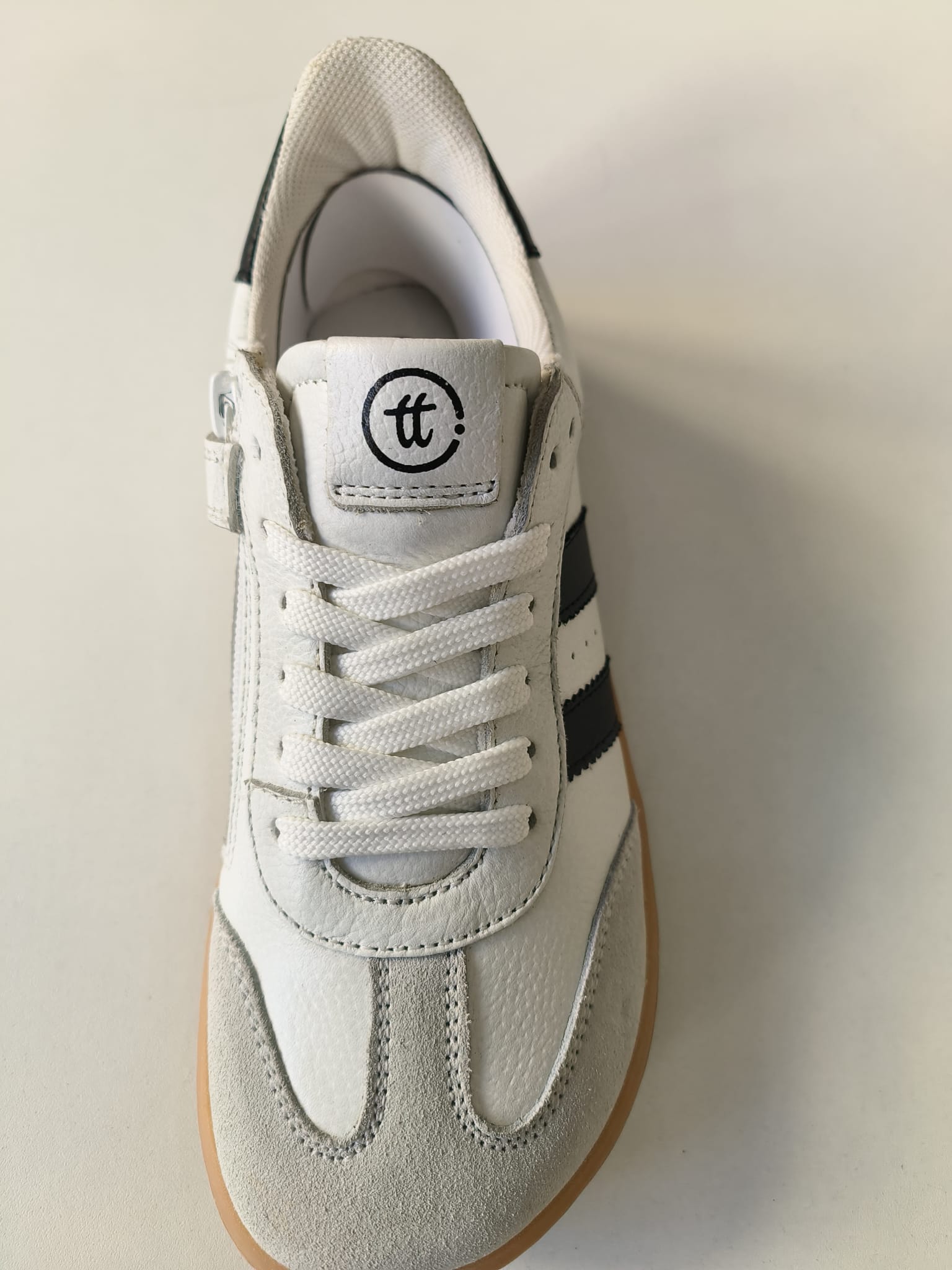 Detalhe da frente da sapatilha Chetto, mostrando os atacadores brancos, a ponteira cinza e o logótipo 'tt' na lingueta.