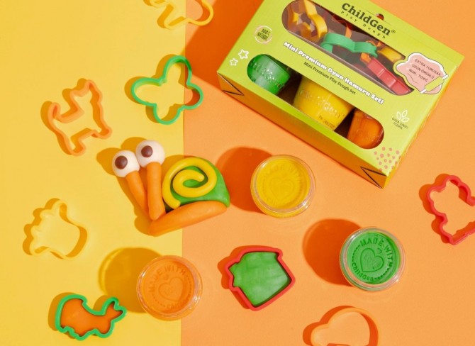 Composição de brincadeira com plasticina ChildGen, mostrando potes abertos, peças moldadas como um caracol e vários cortadores de formas espalhados sobre um fundo amarelo e laranja.