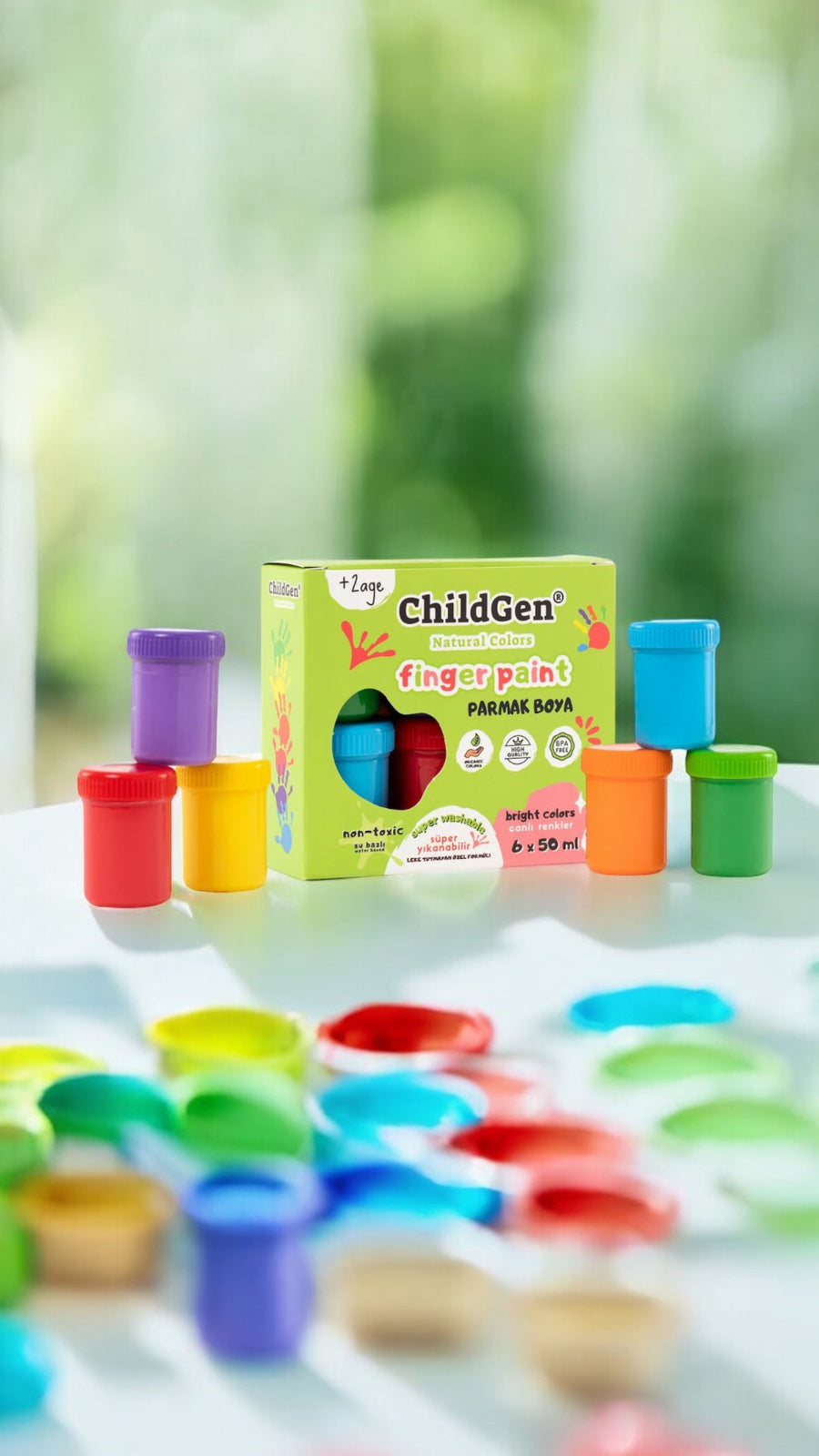 Caixa de tintas ChildGen com vários potes de tinta coloridos dispostos em primeiro plano sobre uma superfície branca, com fundo desfocado de natureza.