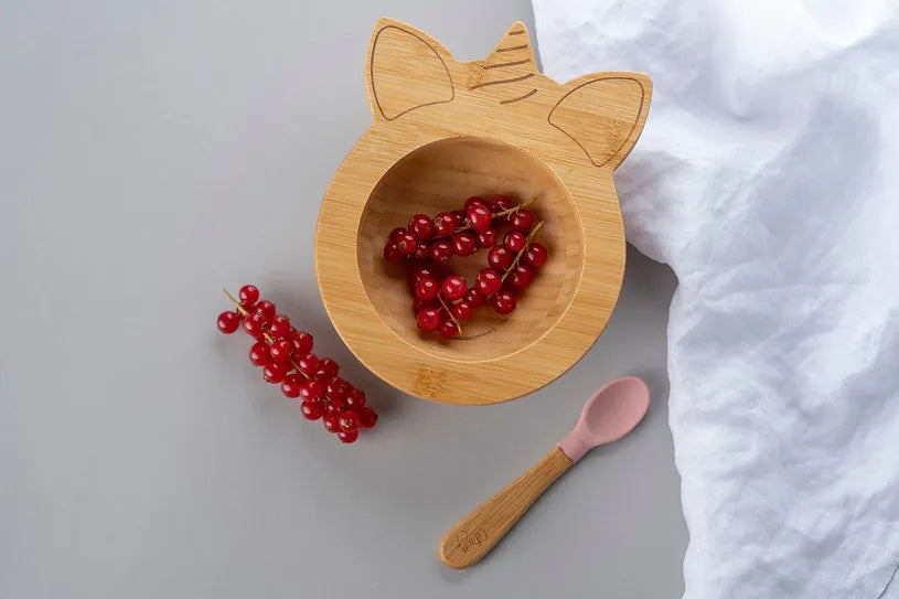 Tigela de bambu Citron em forma de unicórnio com groselhas vermelhas e colher rosa, sobre fundo cinzento.