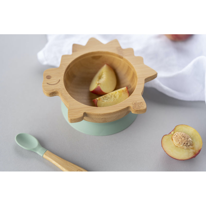 Tigela de bambu Citron com pedaços de pêssego, colher de bambu ao lado, sobre fundo cinzento.