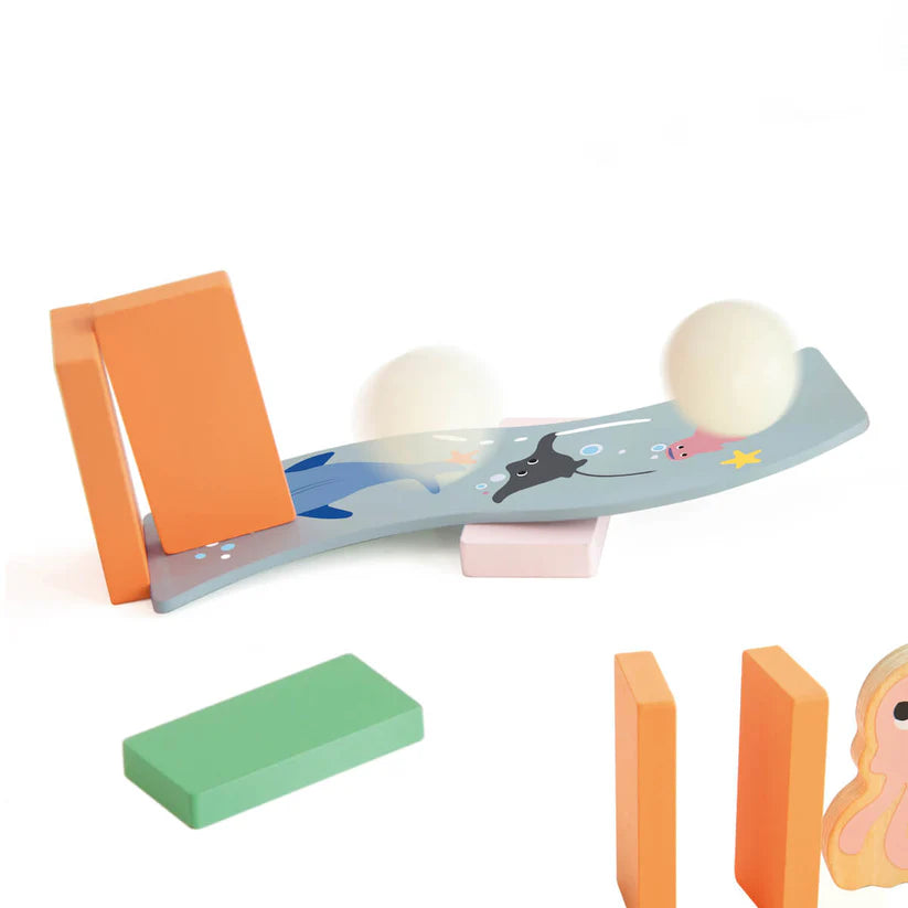 Detalhe do mecanismo de dominó com uma rampa curva decorada com vida marinha, ativando bolas brancas em equilíbrio.