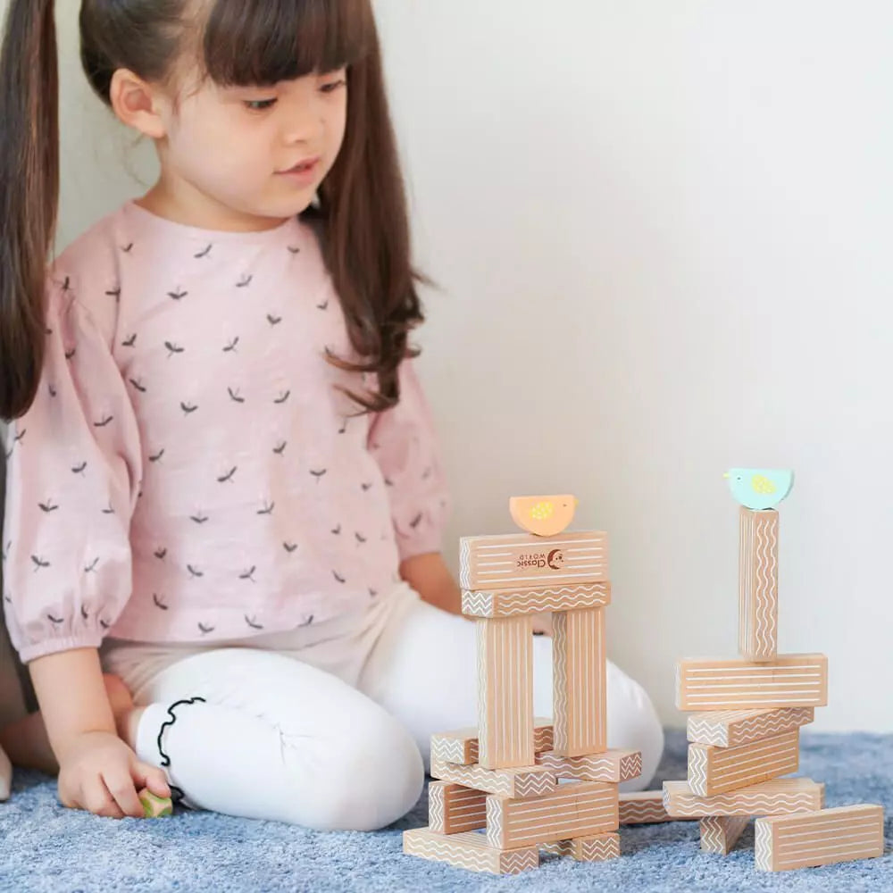 Criança pequena concentrada a empilhar blocos de madeira com padrões, incluindo duas peças de pássaros do Classic World.