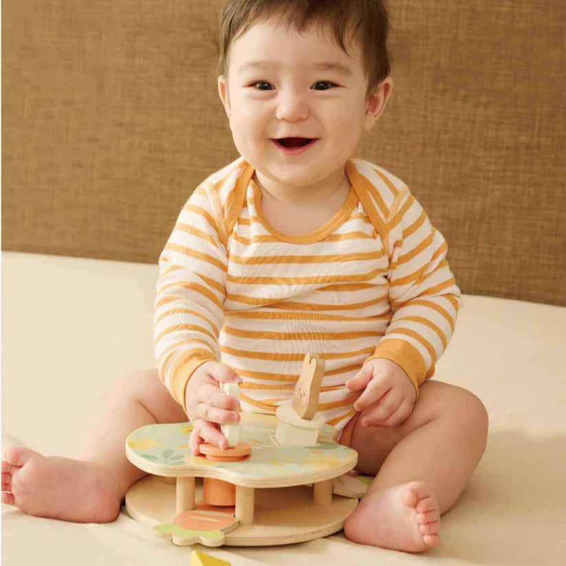 Bebê sorrindo enquanto brinca com o Jogo de encaixe dos Coelhos Classic World, demonstrando o uso e diversão do brinquedo.