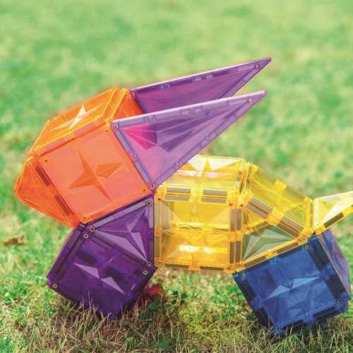 Brincadeira criativa com blocos magnéticos Clever Clixx coloridos (roxo, laranja, amarelo, azul) montados sobre relva verde.