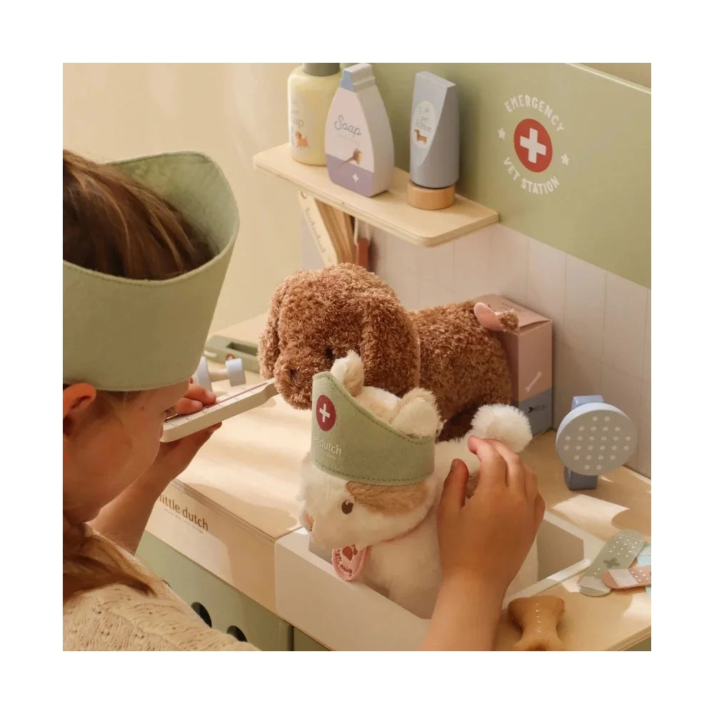 Close-up de uma criança a usar a clínica veterinária, focando no lavatório onde um peluche de gato está a ser tratado, com vários produtos de higiene ao fundo.