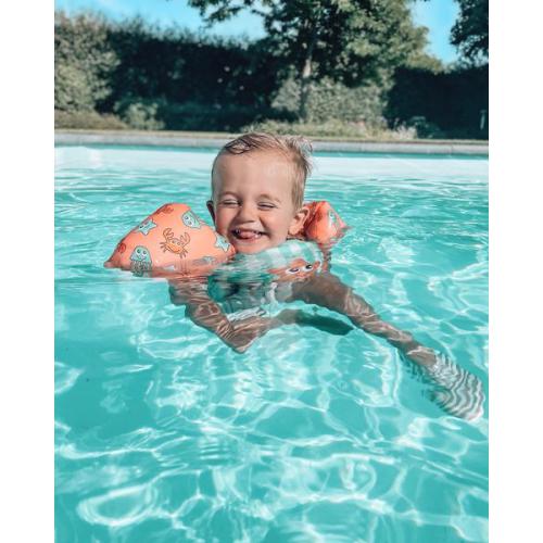 Criança a brincar na piscina usando o colete de flutuação Swim Essentials, com padrão de criaturas marinhas.