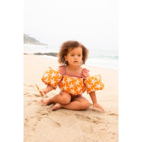Criança na praia usando o colete de flutuação Swim Essentials com padrão de estrelas-do-mar laranja.