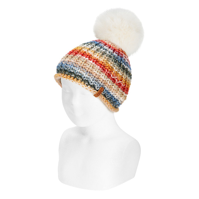 Gorro Condor de malha com padrão arco-íris vibrante e pompom grande em pelo sintético branco, visto num manequim.