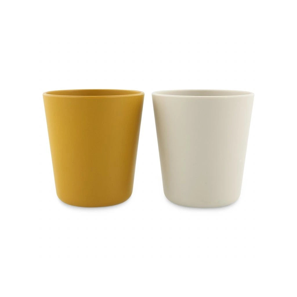 Conjunto de dois copos infantis, um amarelo mostarda e outro branco creme, feitos de plástico vegetal.