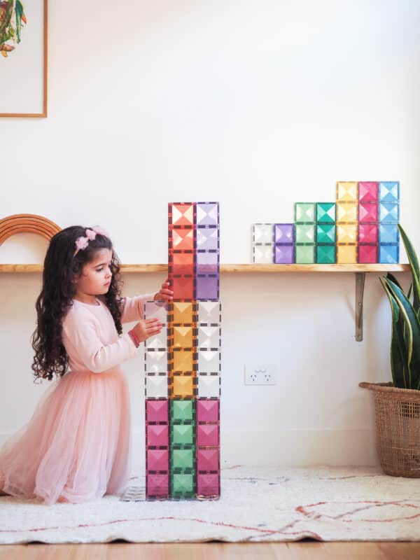 Criança a adicionar um bloco a uma construção alta de Connetix Pastel Rectangle.
