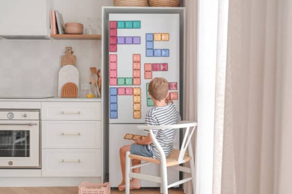 Criança a colocar blocos Connetix Pastel Rectangle no frigorífico, criando um padrão.