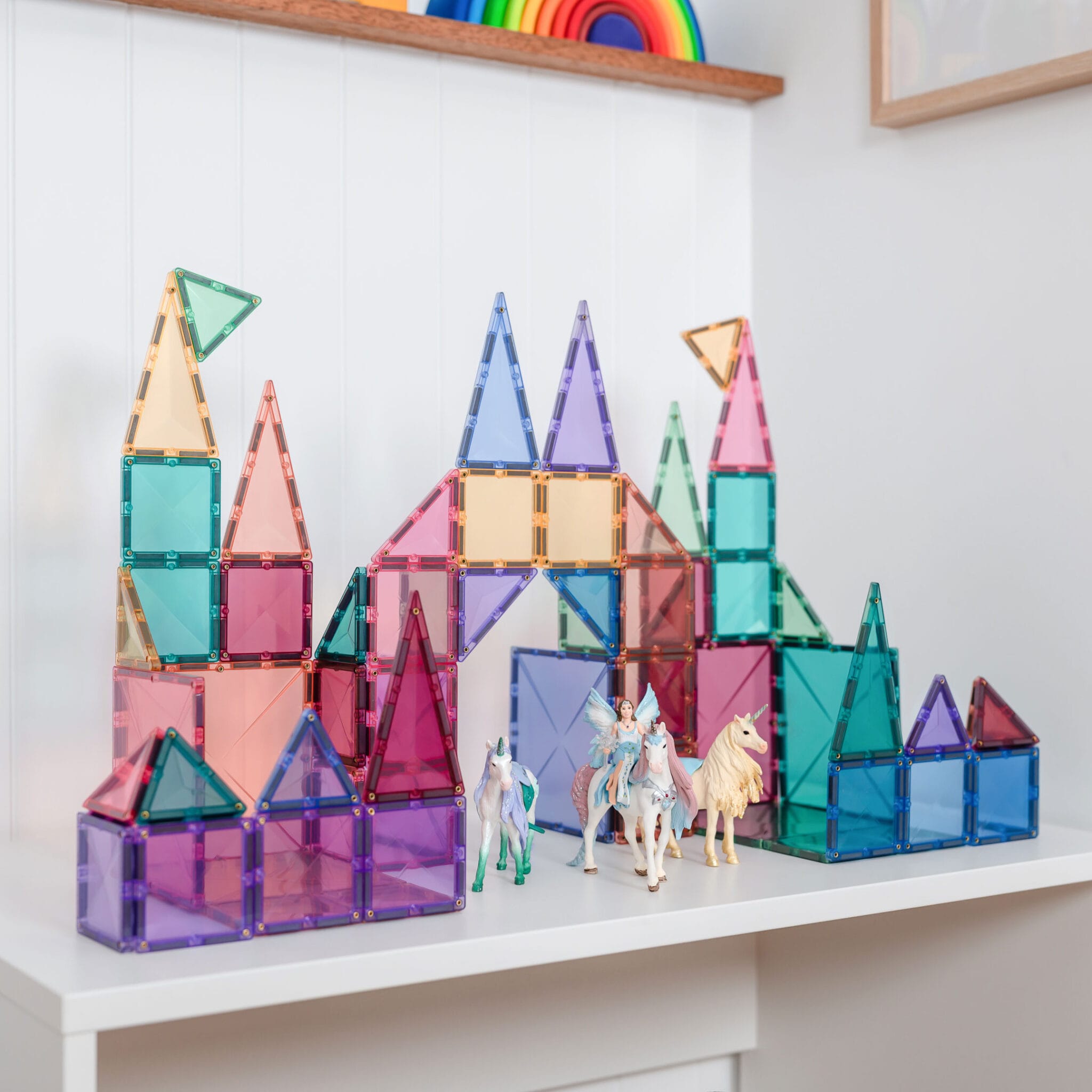 Construção de um castelo com arco e torres feita com blocos Connetix Pastel, com figuras de fantasia à frente.