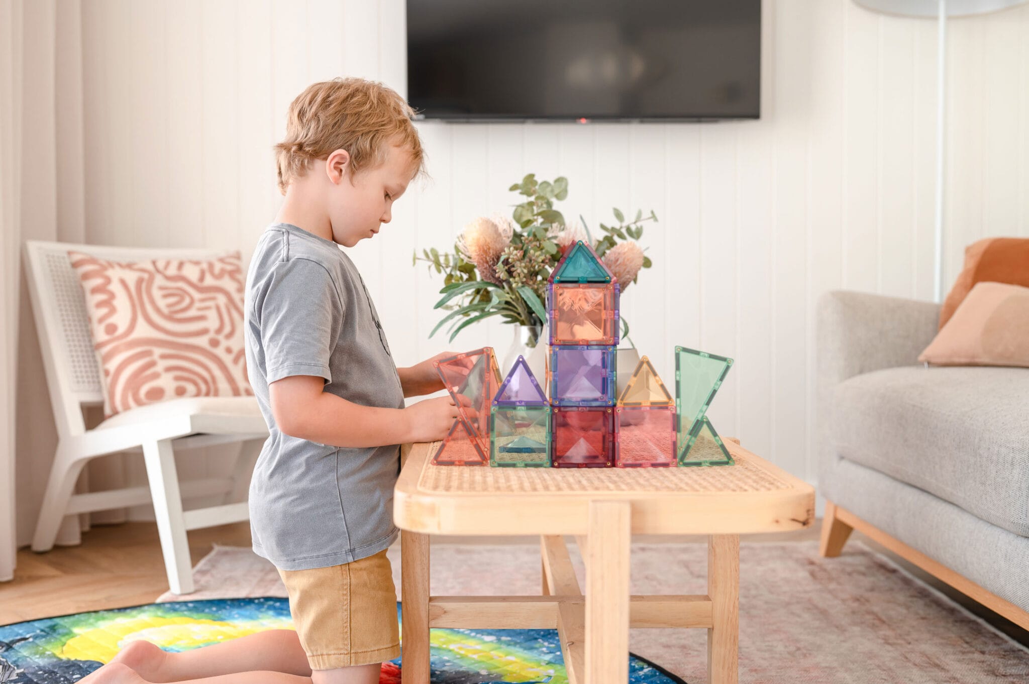 Criança a brincar e a construir com blocos magnéticos Connetix Pastel numa mesa baixa.
