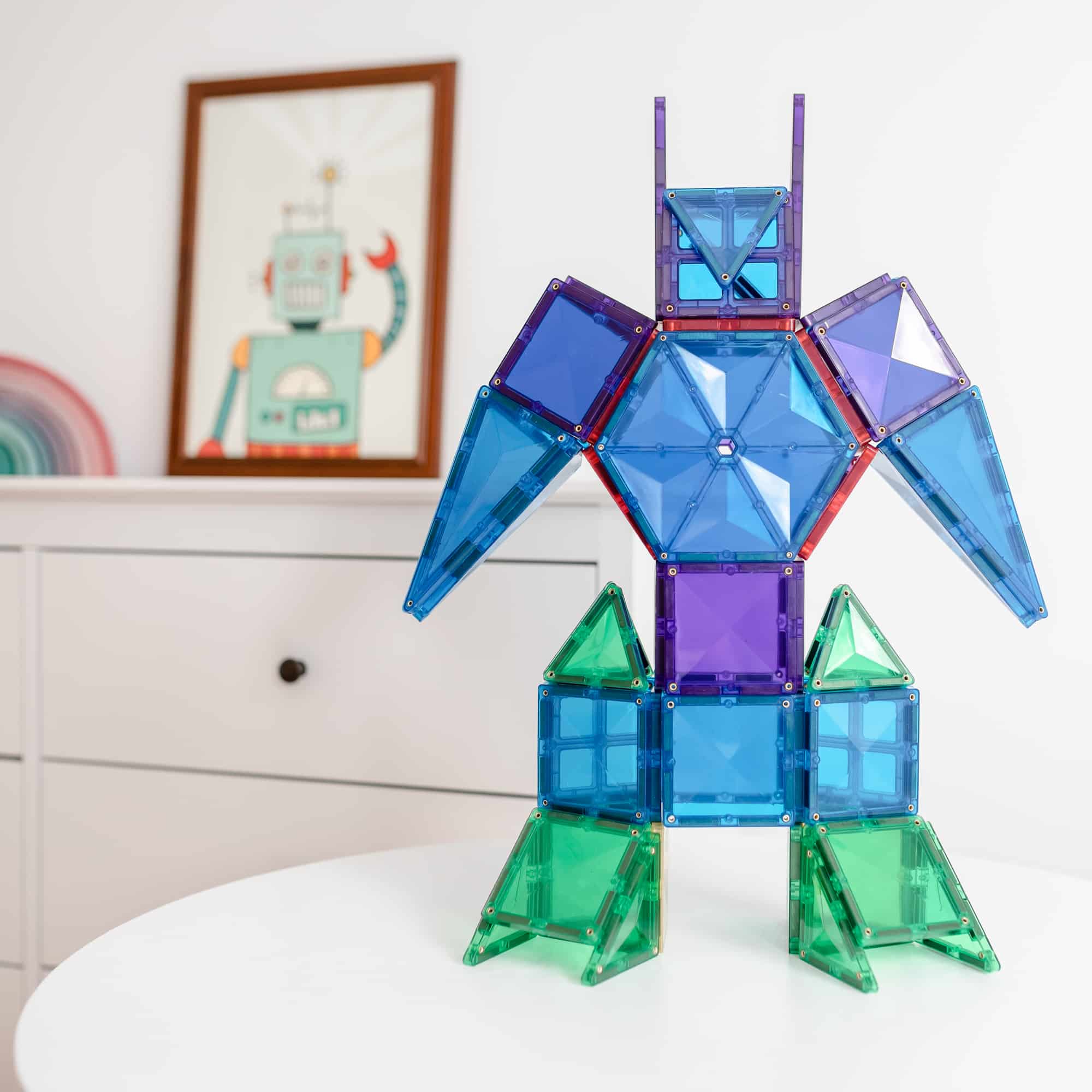 Robô colorido construído com blocos magnéticos Connetix Rainbow ao lado de um quadro.