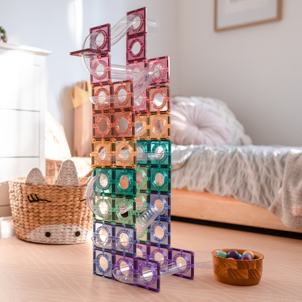 Torre alta de pista de bolas magnética Connetix em tons pastel e transparentes, montada num quarto, com uma taça de bolas no chão.