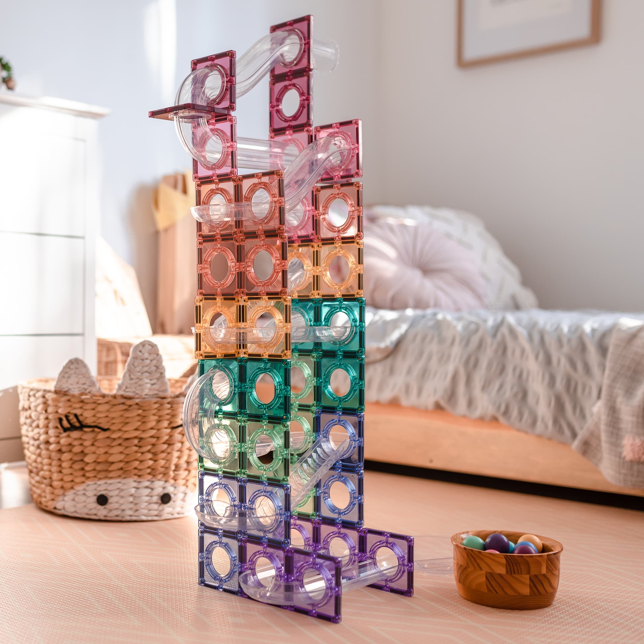 Torre alta de pista de bolas magnética Connetix em tons pastel e transparentes, montada num quarto, com uma taça de bolas no chão.