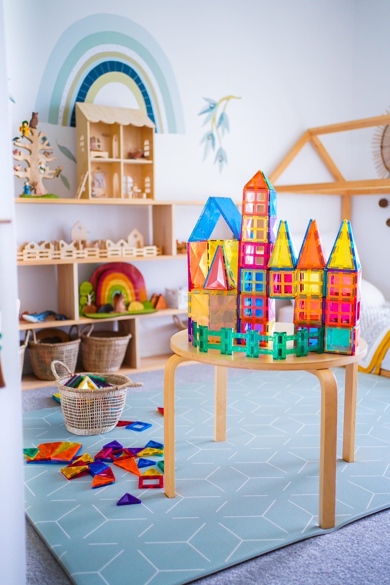 Construção elaborada de um castelo com telhados pontiagudos usando blocos magnéticos Connetix, exposta numa mesa num quarto infantil decorado.