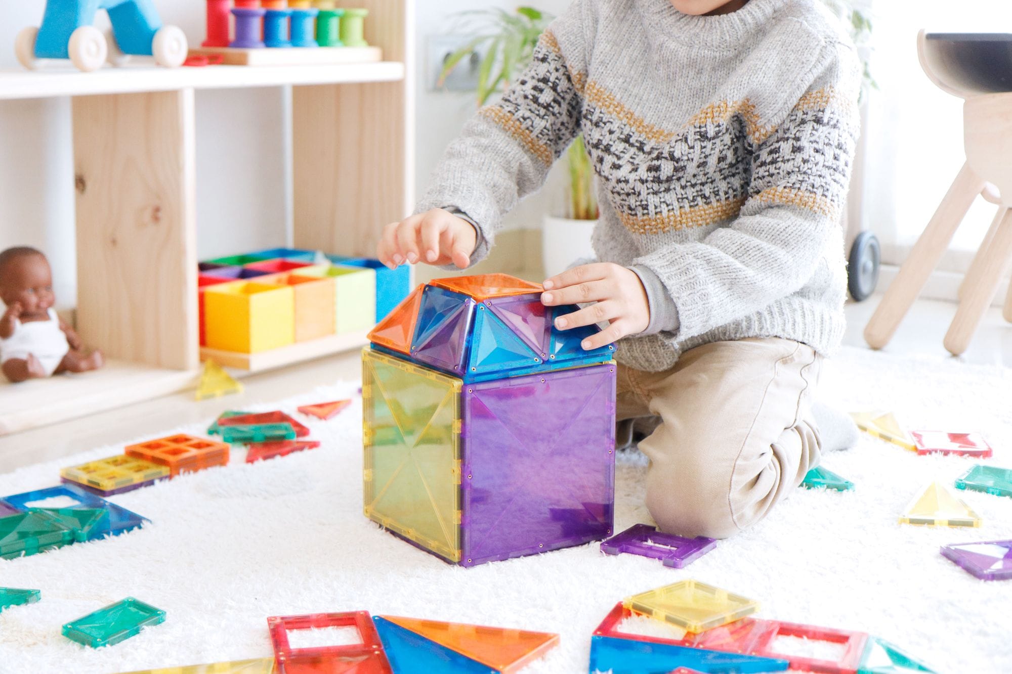 Foco nas mãos de uma criança a construir uma estrutura cúbica com blocos magnéticos Connetix coloridos, promovendo a aprendizagem STEAM.