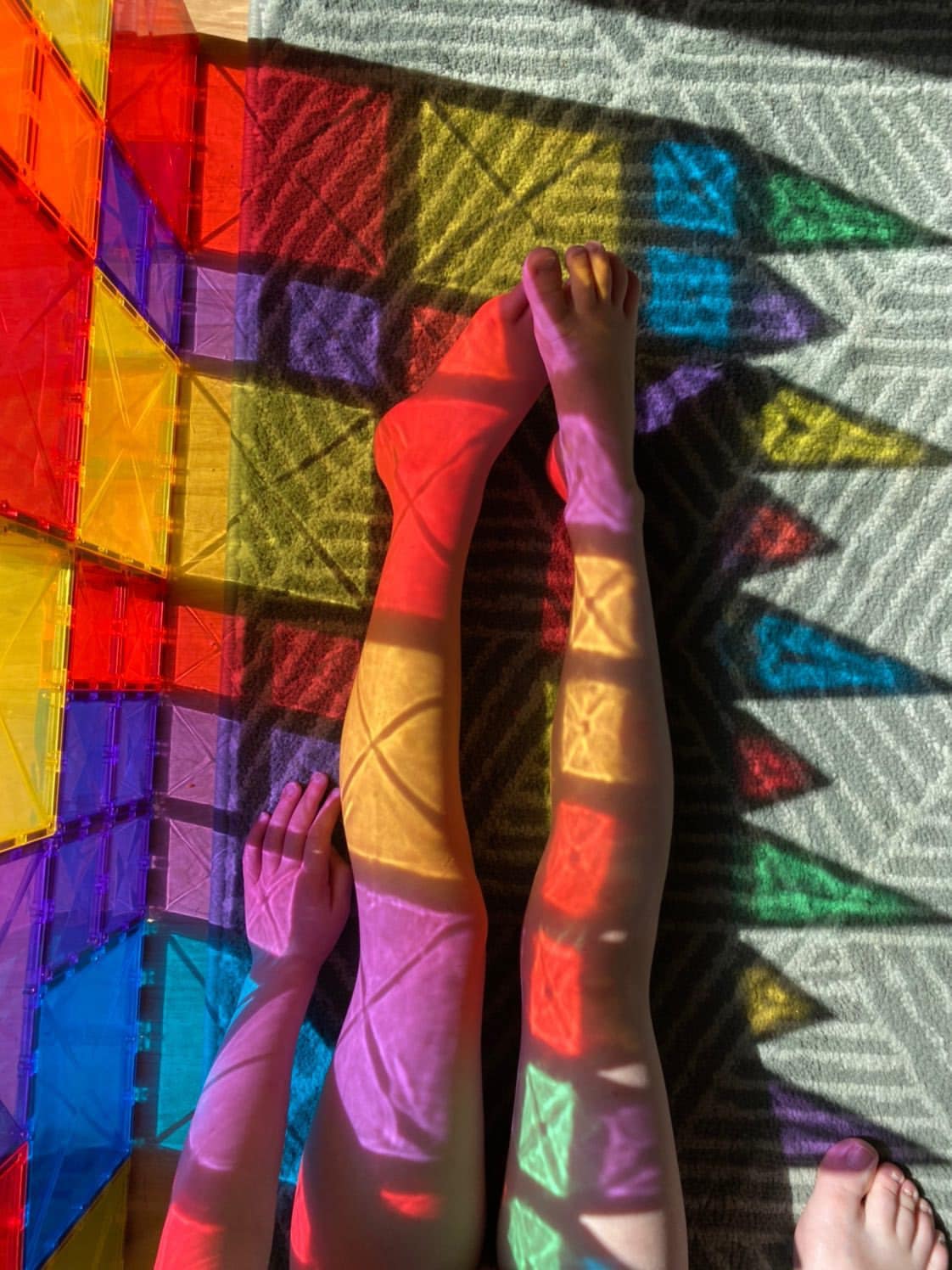 Pernas e mãos com refrações de luz coloridas dos blocos magnéticos Connetix Rainbow Creative.