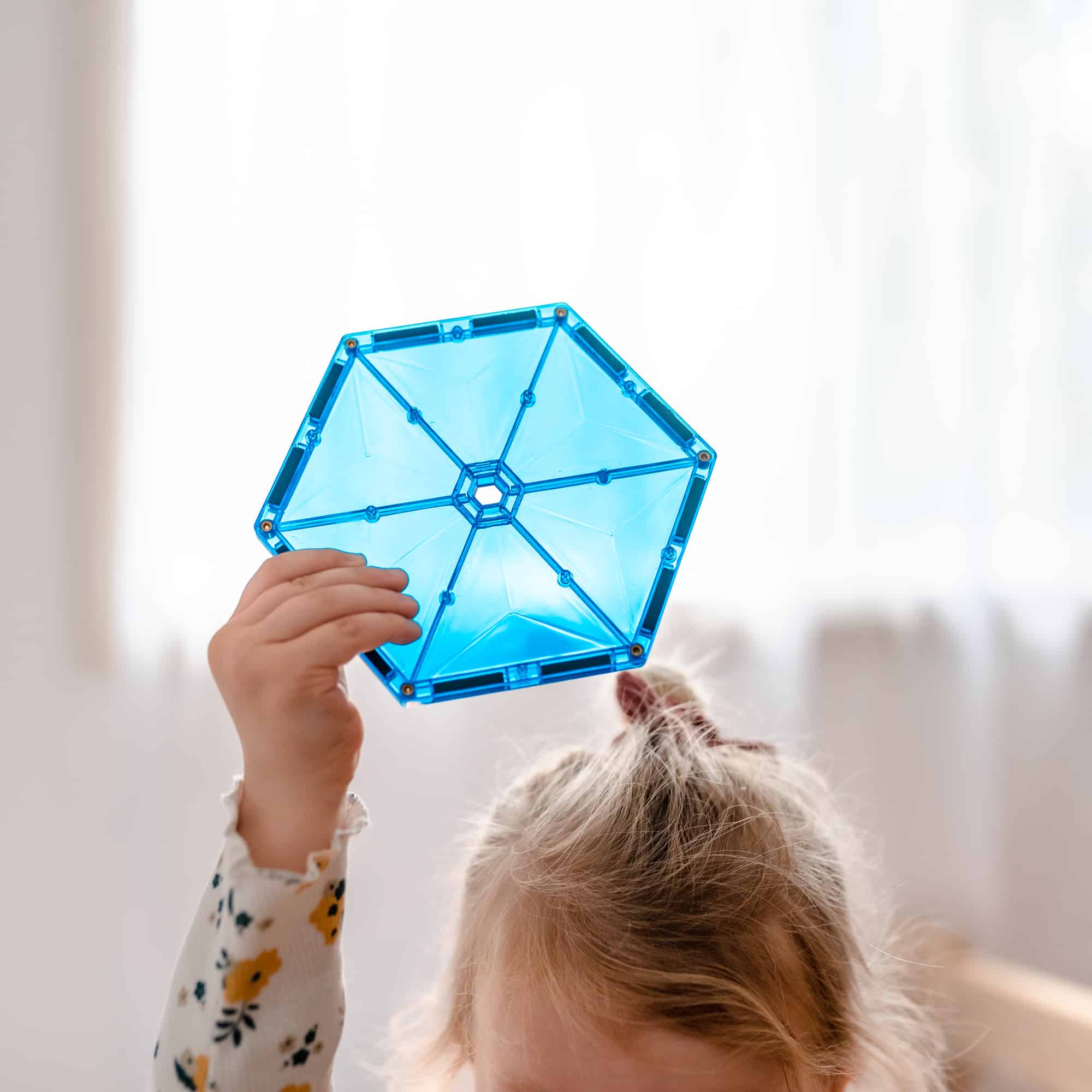 Criança a segurar um hexágono magnético Connetix azul transparente contra a luz.