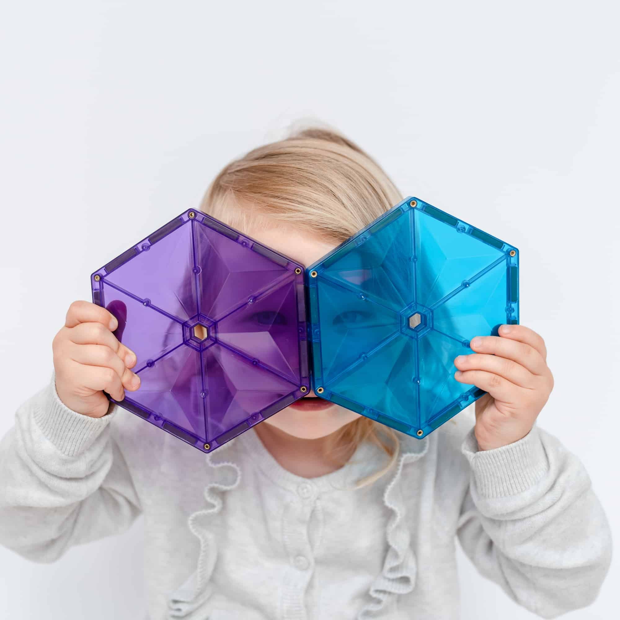 Criança a segurar dois hexágonos magnéticos Connetix coloridos (roxo e azul) à frente dos olhos.